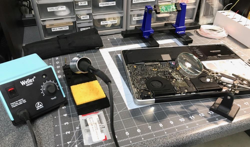 Weller soldering station and magnifying glass at workbench with 2011 MacBook Pro