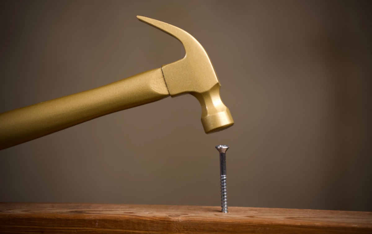 Golden hammer driving a screw into a board